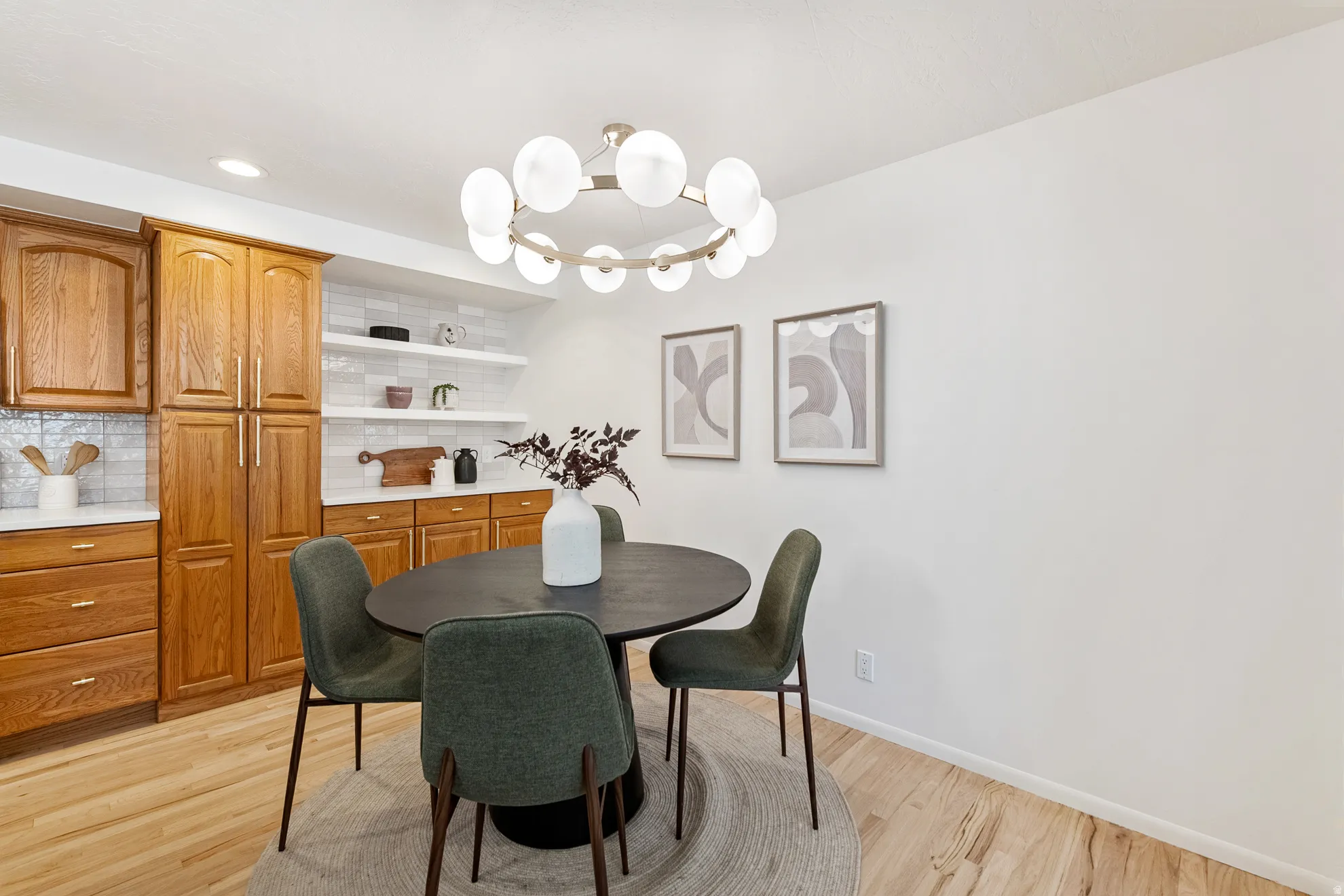 Hardwood flooring, kitchen cabinetry with integrated pantry storage, white subway tile backsplash, white countertops, and a modern circular chandelier
