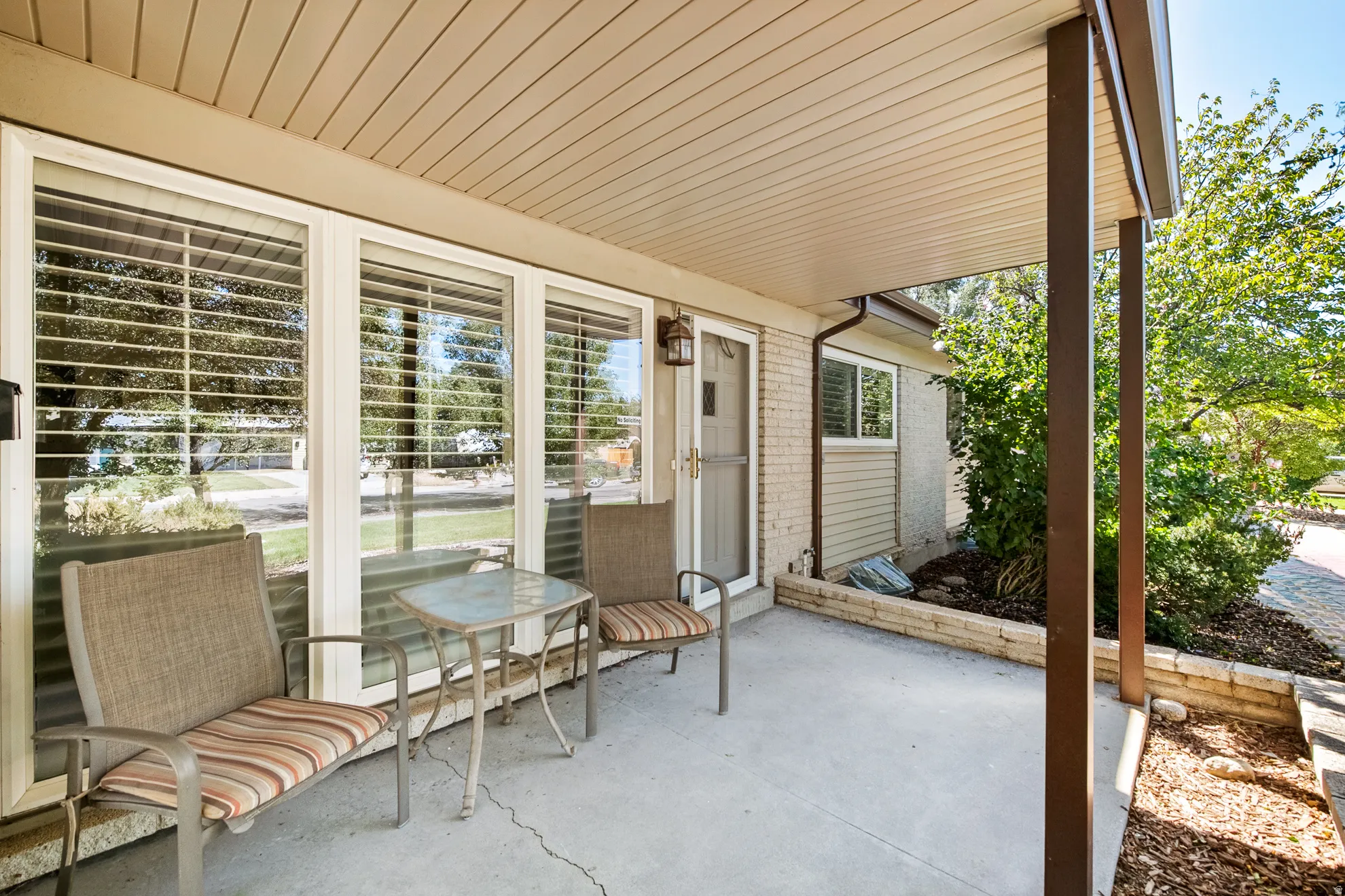 Covered concrete patio with white framed windows, exterior lighting fixture, and a brick base planter