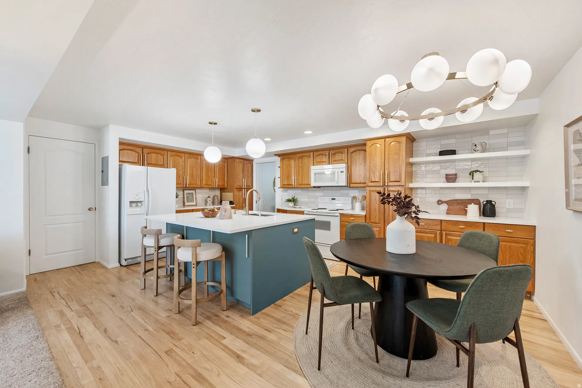 Spacious updated kitchen featuring a central island with a white countertop, wood-finish flooring, white tile backsplash, and wood cabinetry