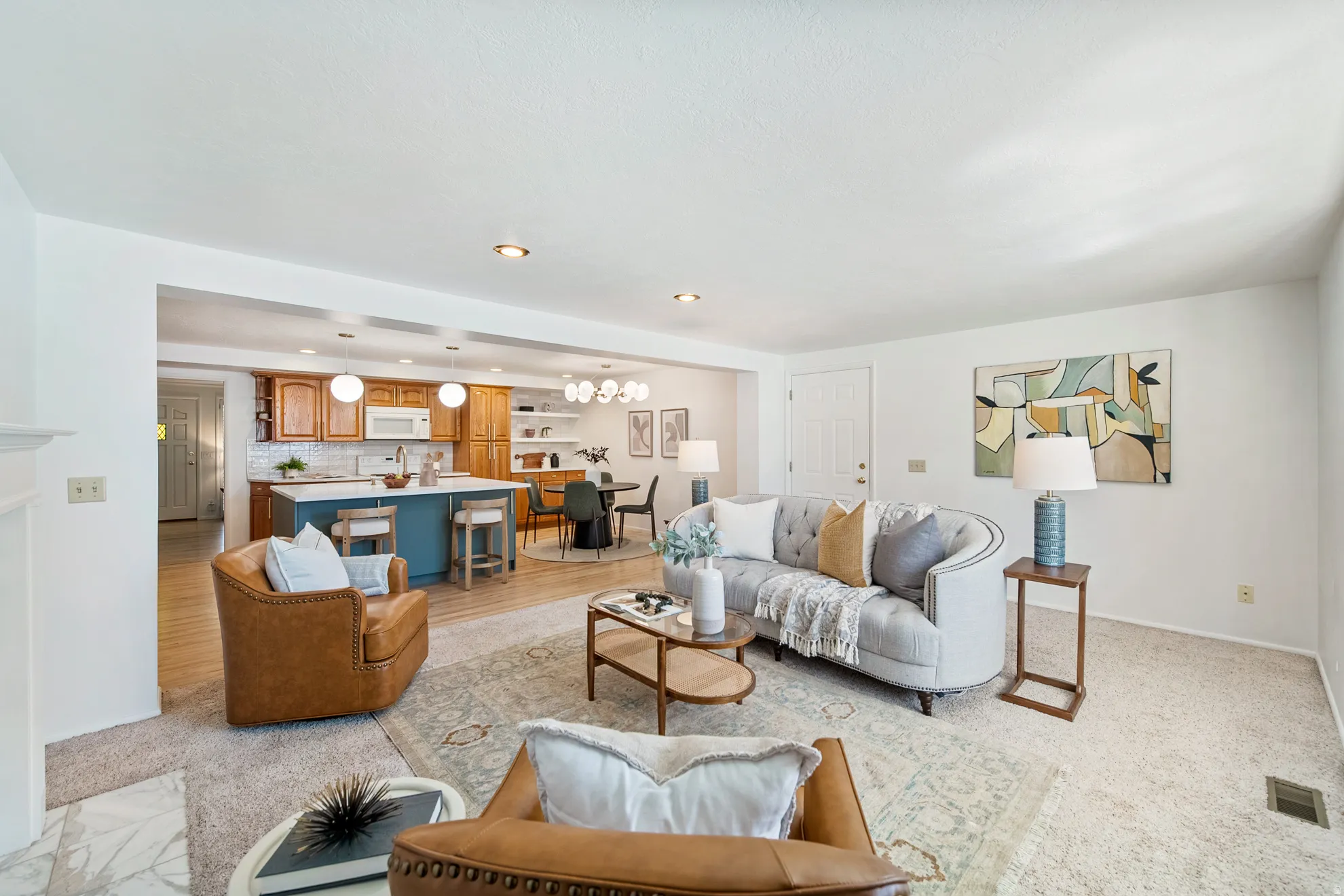 Open-concept living area with carpeted flooring leading to hardwood-finish flooring in the kitchen and dining areas