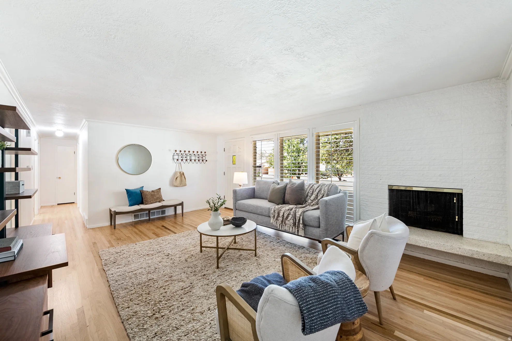 Wood-finish flooring, white brick fireplace with hearth, and window shutters