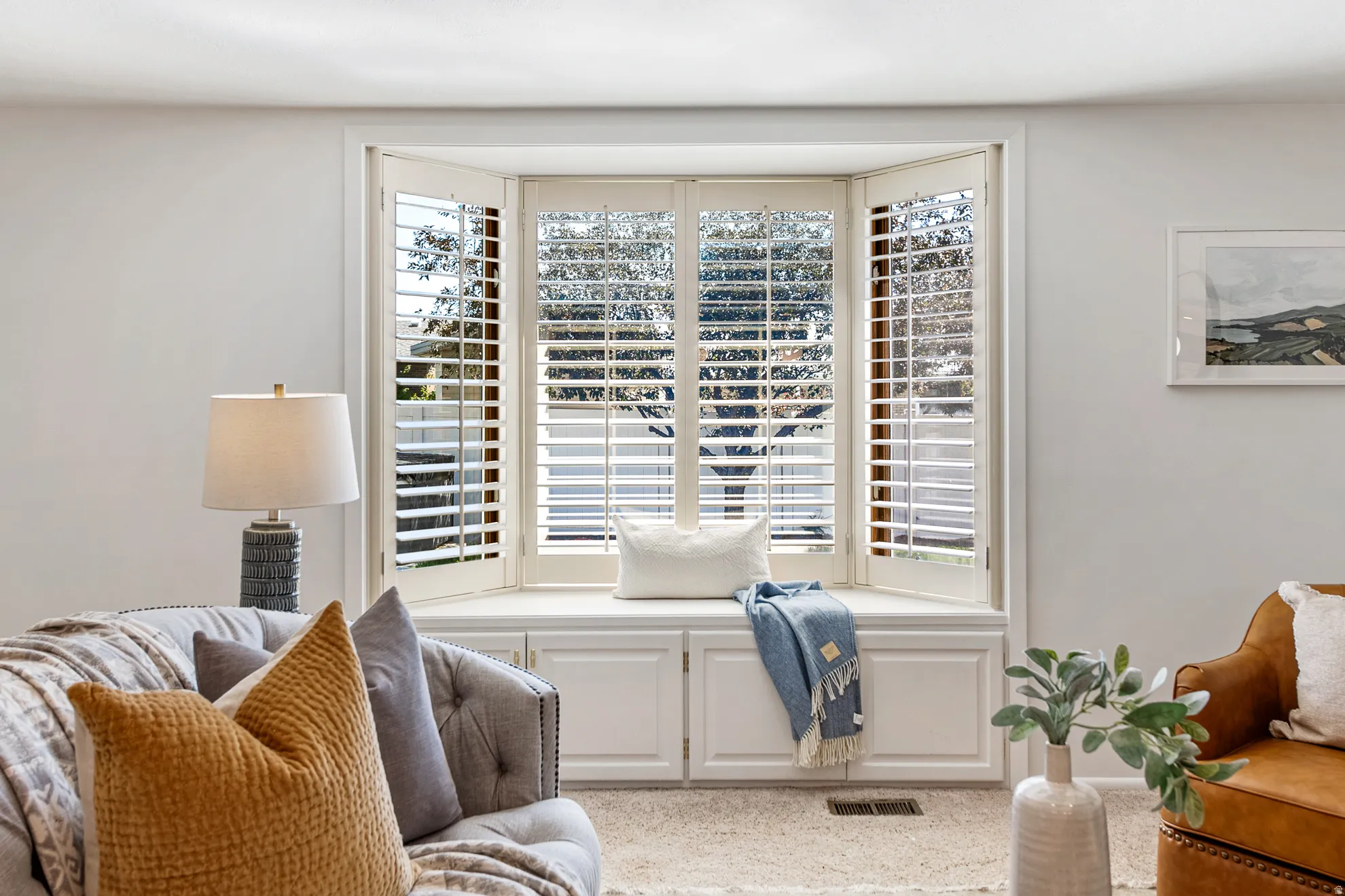 Bay window with built-in bench seating and storage cabinetry, featuring plantation shutters