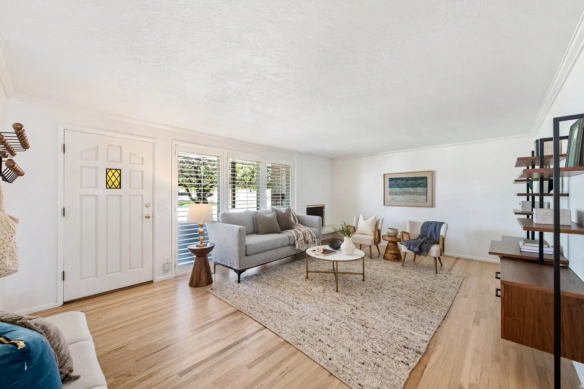 Light wood-finish flooring, white paneled door with decorative glass insert, plantation shutters, crown molding, and built-in shelving unit