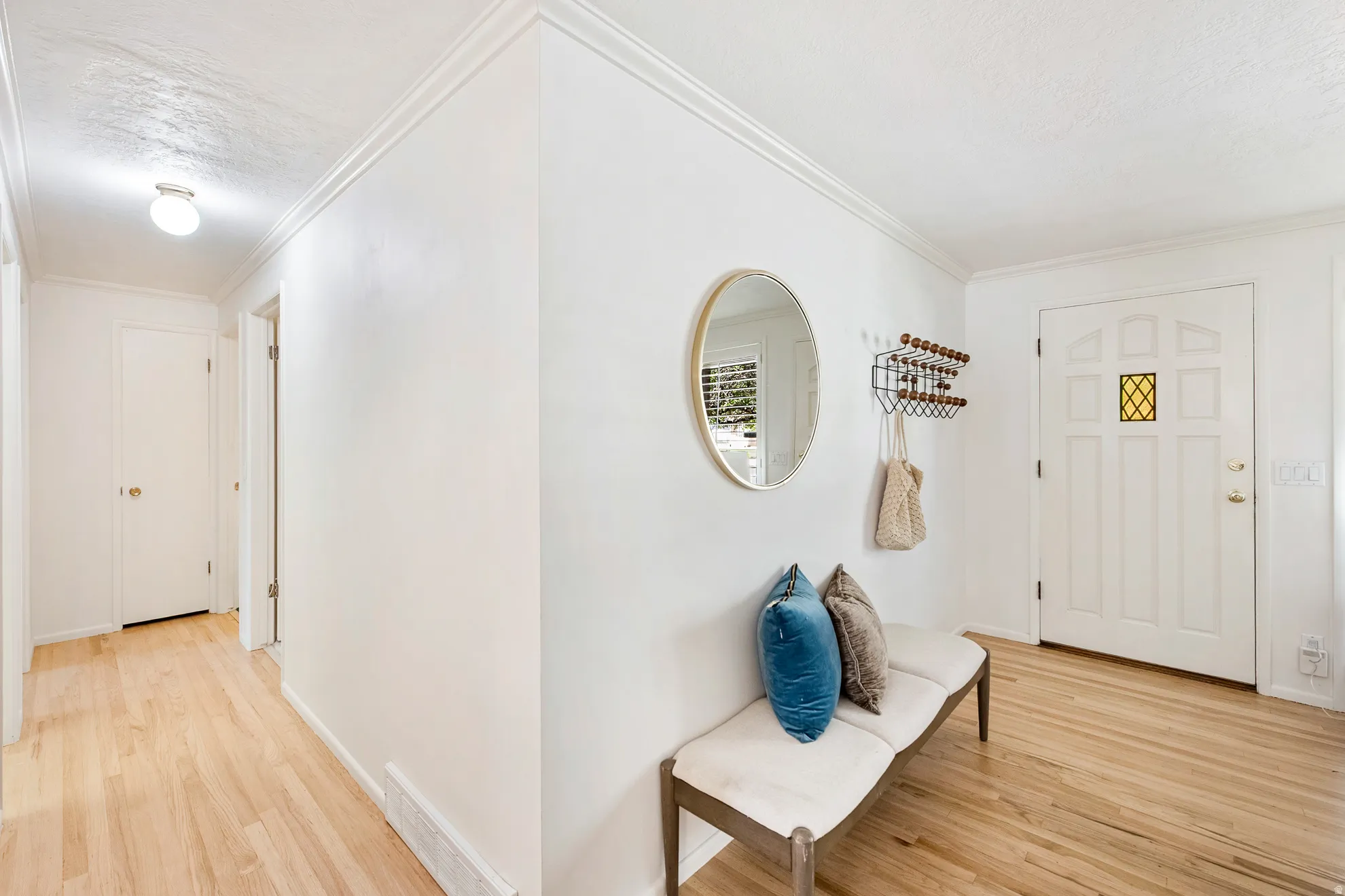 Light wood-finish flooring, white paneled entry door with decorative glass inlay, textured ceiling, and crown molding