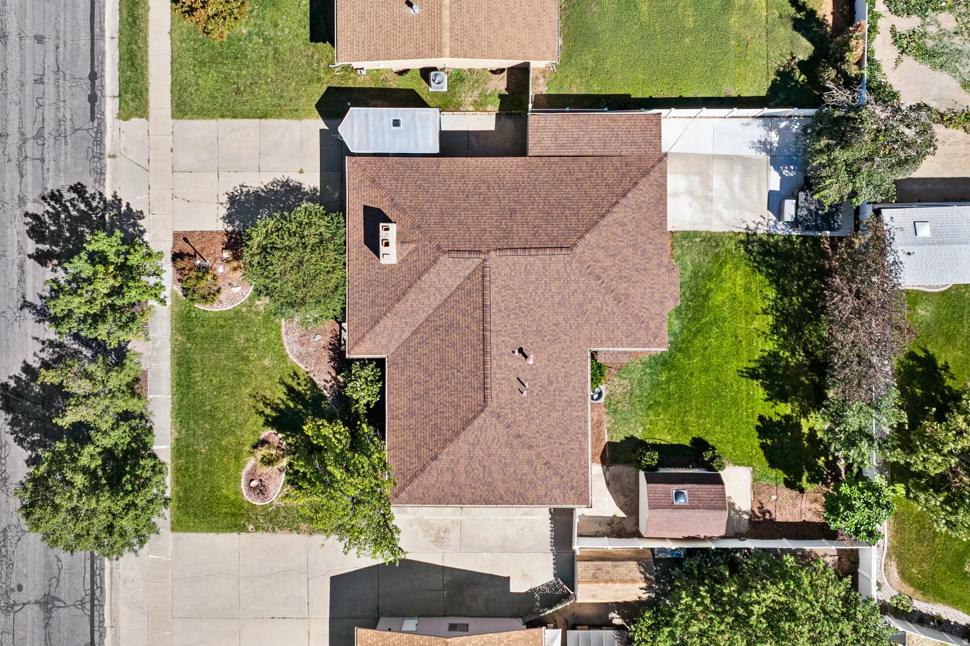 Asphalt shingle roofing with a chimney, concrete driveway, and mature landscaping
