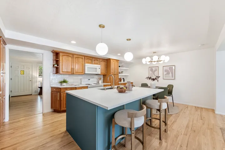 Light wood-finish flooring, white countertops, wood cabinetry, white subway tile backsplash, and a blue kitchen island with seating