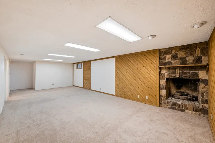 Spacious room featuring a stone fireplace with a wood mantle, wood paneling, recessed lighting, and rectangular ceiling lights