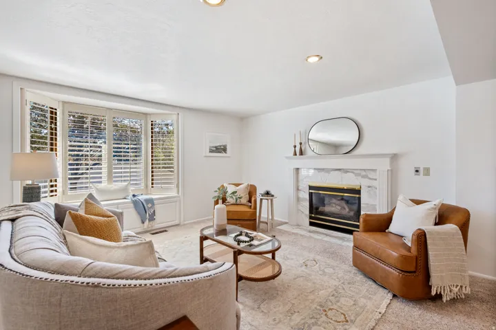 Bay window with plantation shutters and window seat, recessed lighting, fireplace with marble-look surround and white mantel, and neutral carpet