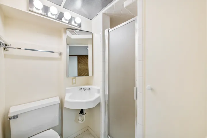 Bathroom featuring a shower enclosure with a frosted glass door, a wall-mounted sink, and a mirrored medicine cabinet