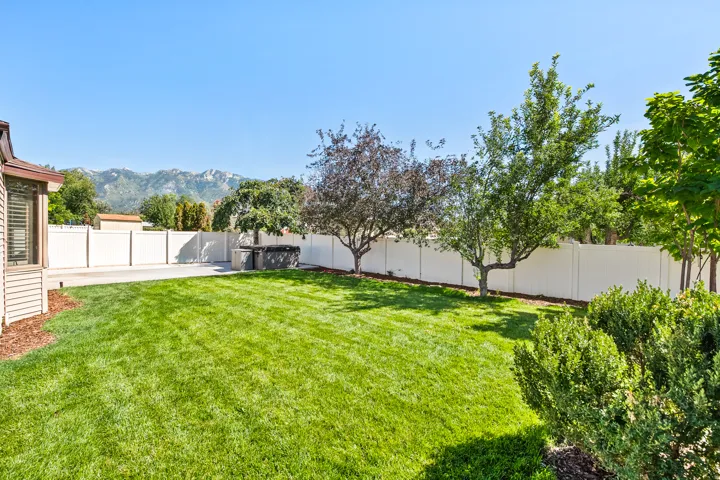 Expansive lawn area with mature trees, surrounded by a privacy fence, and concrete patio space