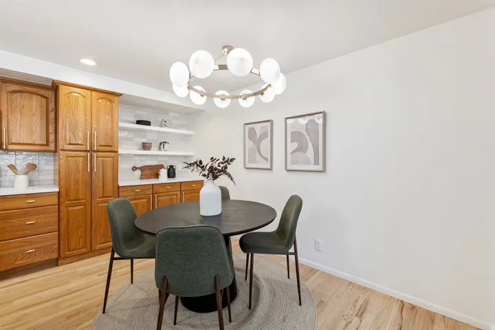 Hardwood flooring, kitchen cabinetry with integrated pantry storage, white subway tile backsplash, white countertops, and a modern circular chandelier