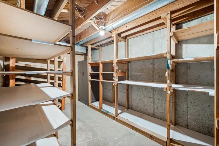 Extensive built-in wood shelving units, concrete flooring, concrete block walls, exposed wood ceiling joists, and a utility cabinet