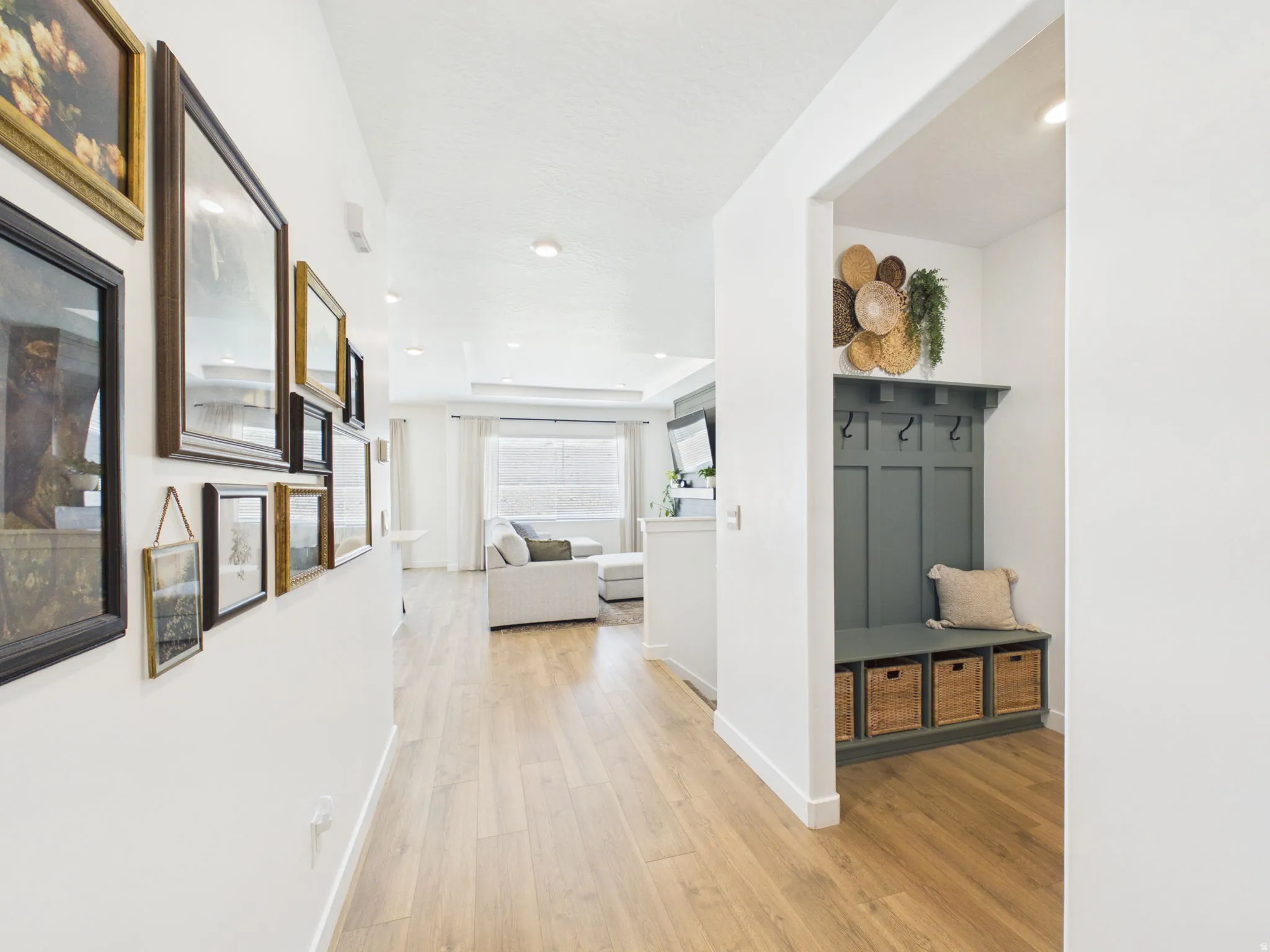 Light wood-finish flooring extending throughout, recessed lighting, and a built-in hall tree with storage baskets