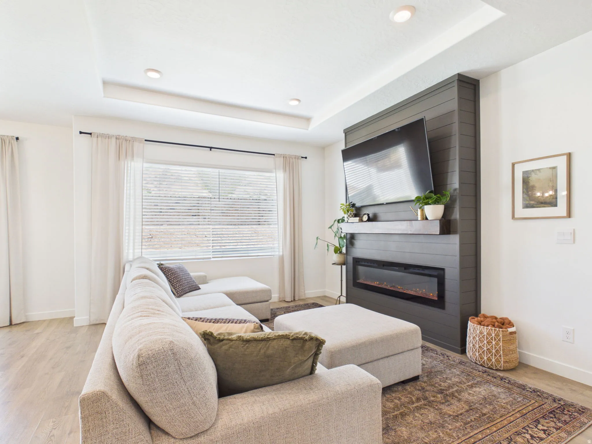 Recessed lighting, tray ceiling, wood-finish flooring, electric fireplace with mantel, and shiplap-accented wall