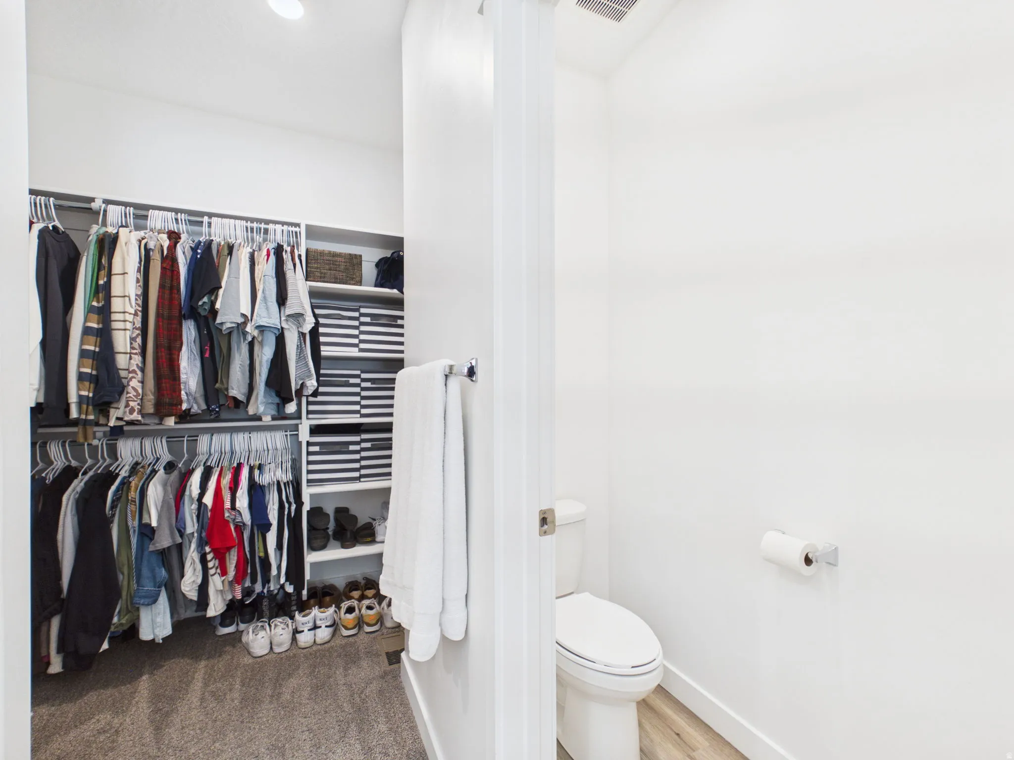 Recessed lighting illuminates the organized closet, featuring white shelving and hanging rods