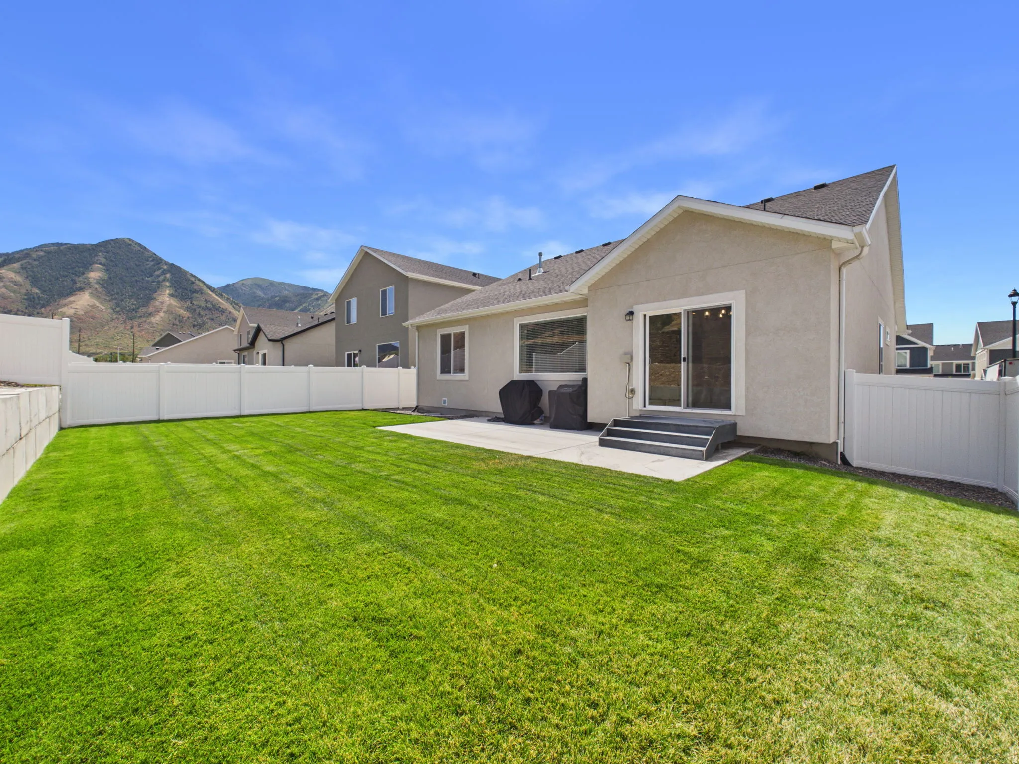 Expansive backyard featuring a manicured lawn, concrete patio, and white privacy fencing