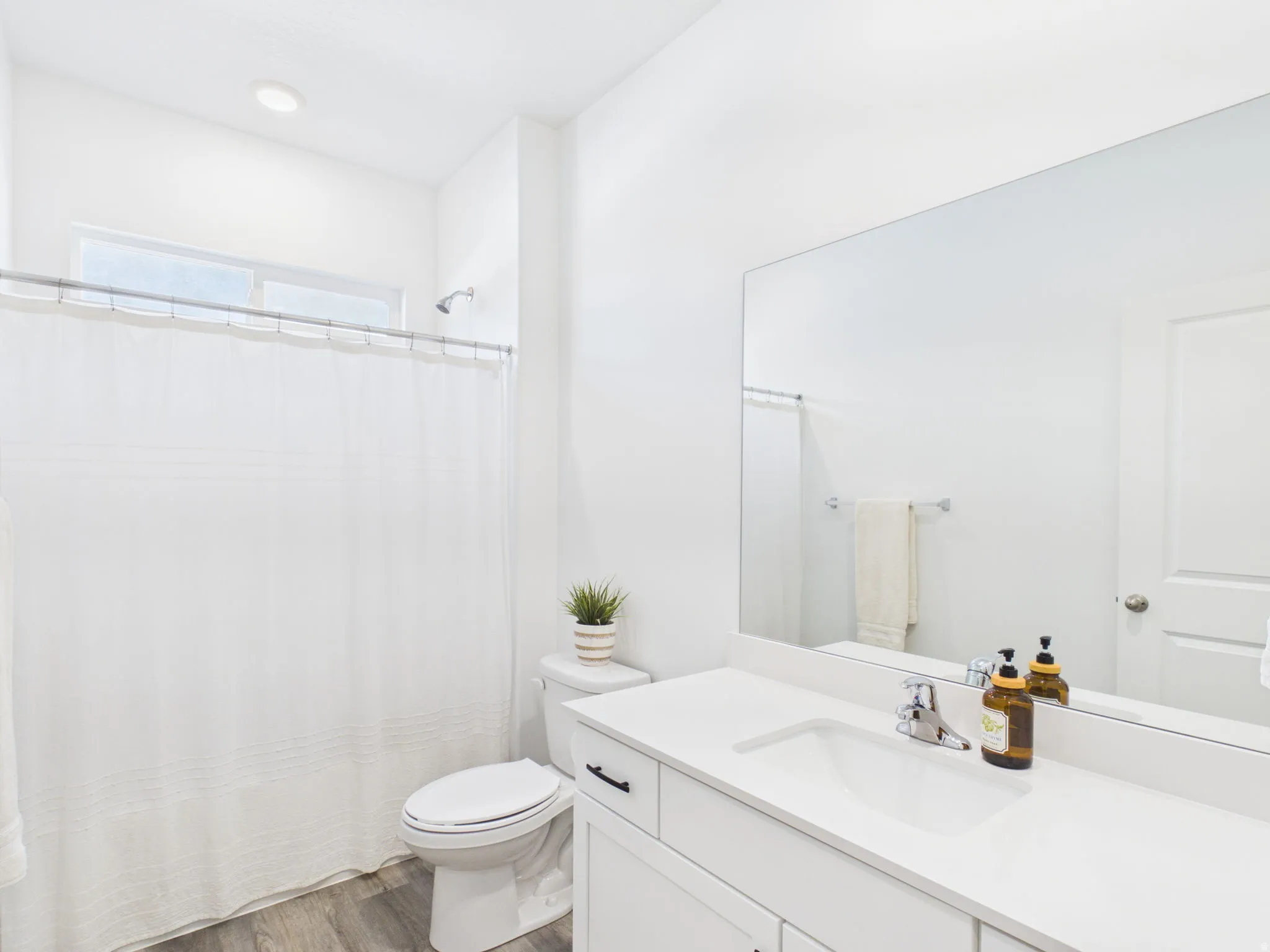 Recessed lighting, wood-finish flooring, white vanity with integrated sink, chrome faucet, and expansive wall mirror