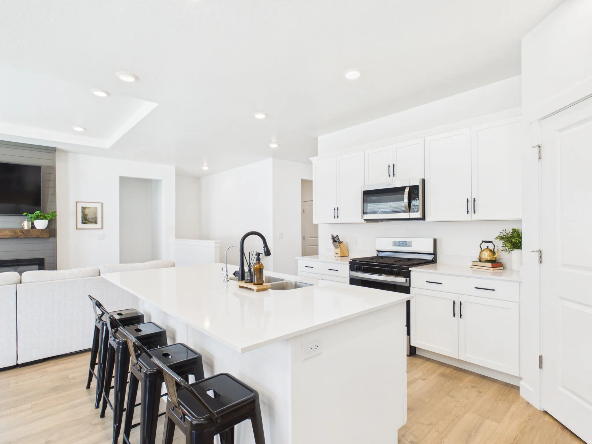 White kitchen cabinetry with stainless steel appliances, a center island featuring an undermount sink and a matte black faucet, and wood-finish flooring