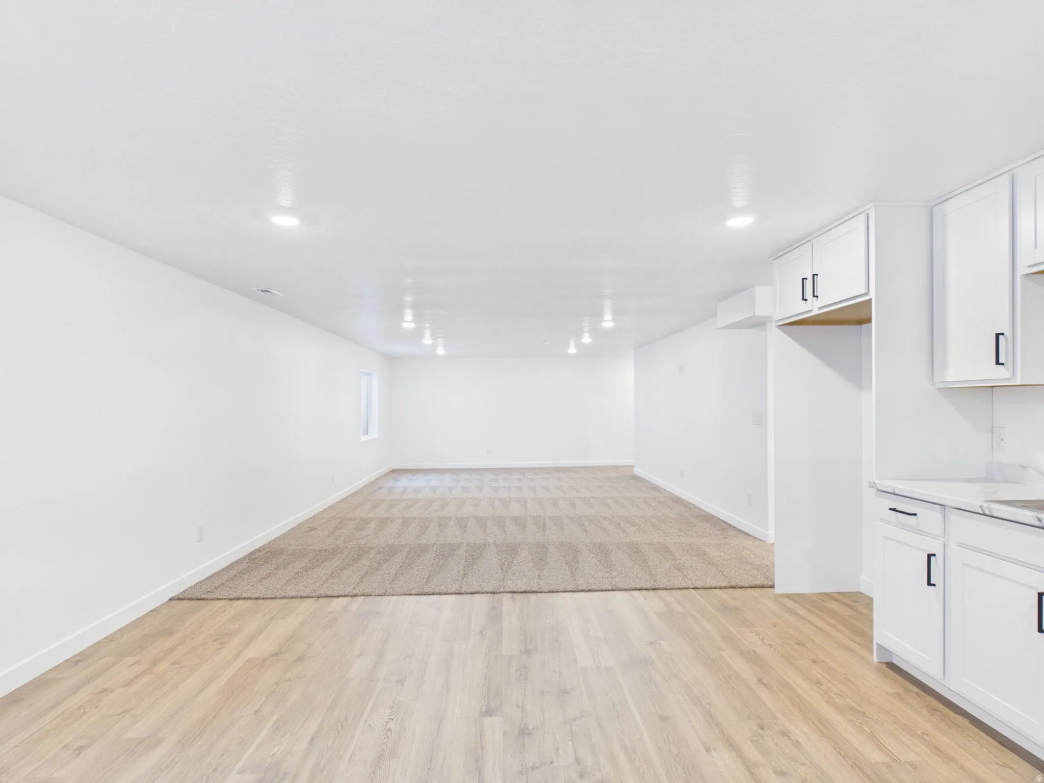 Recessed lighting, wood-finish flooring, white cabinetry with dark hardware, stone-finish countertops, and carpeted area