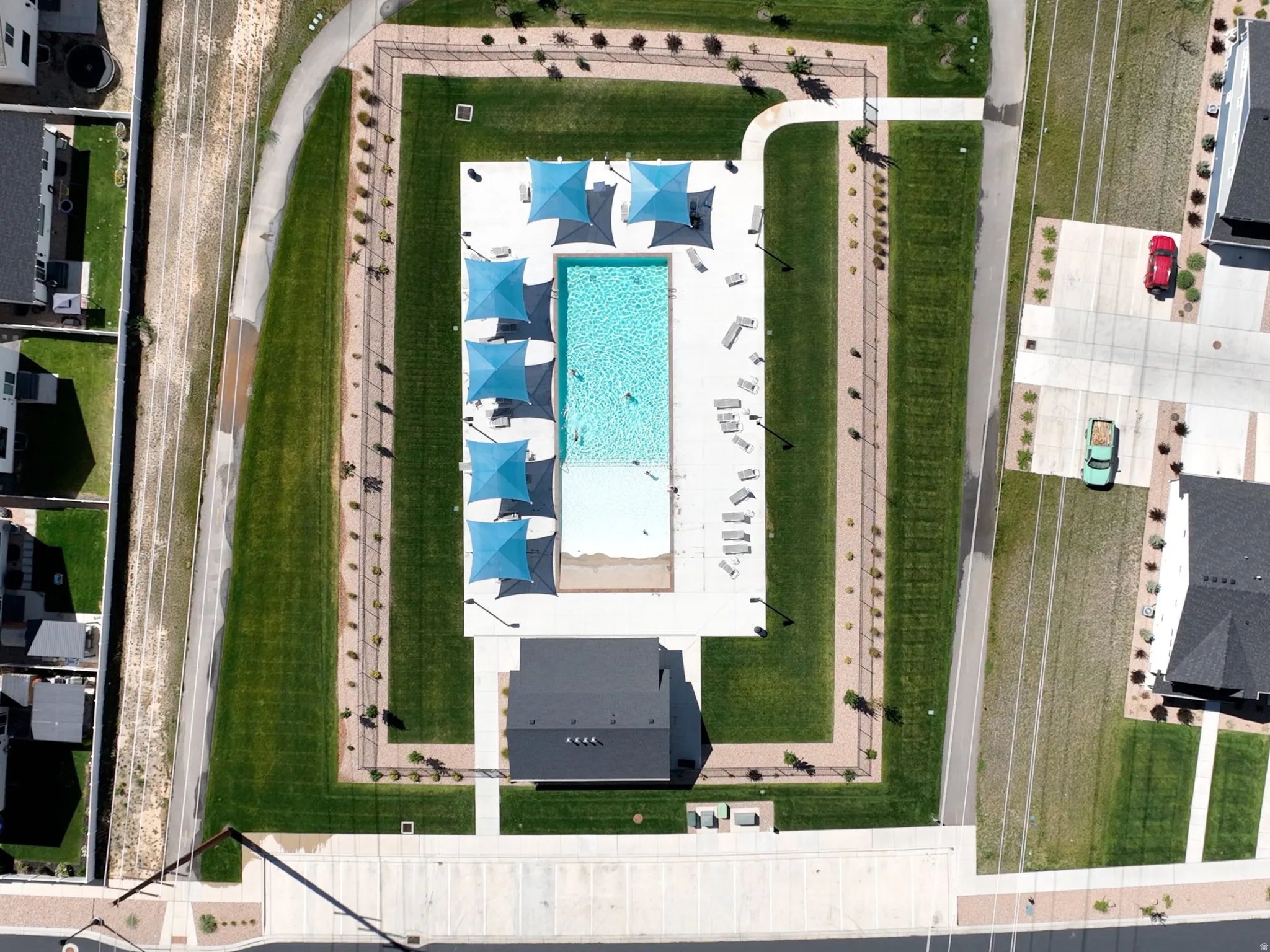 Community swimming pool with sun shades, surrounding paved pathways, and manicured green spaces
