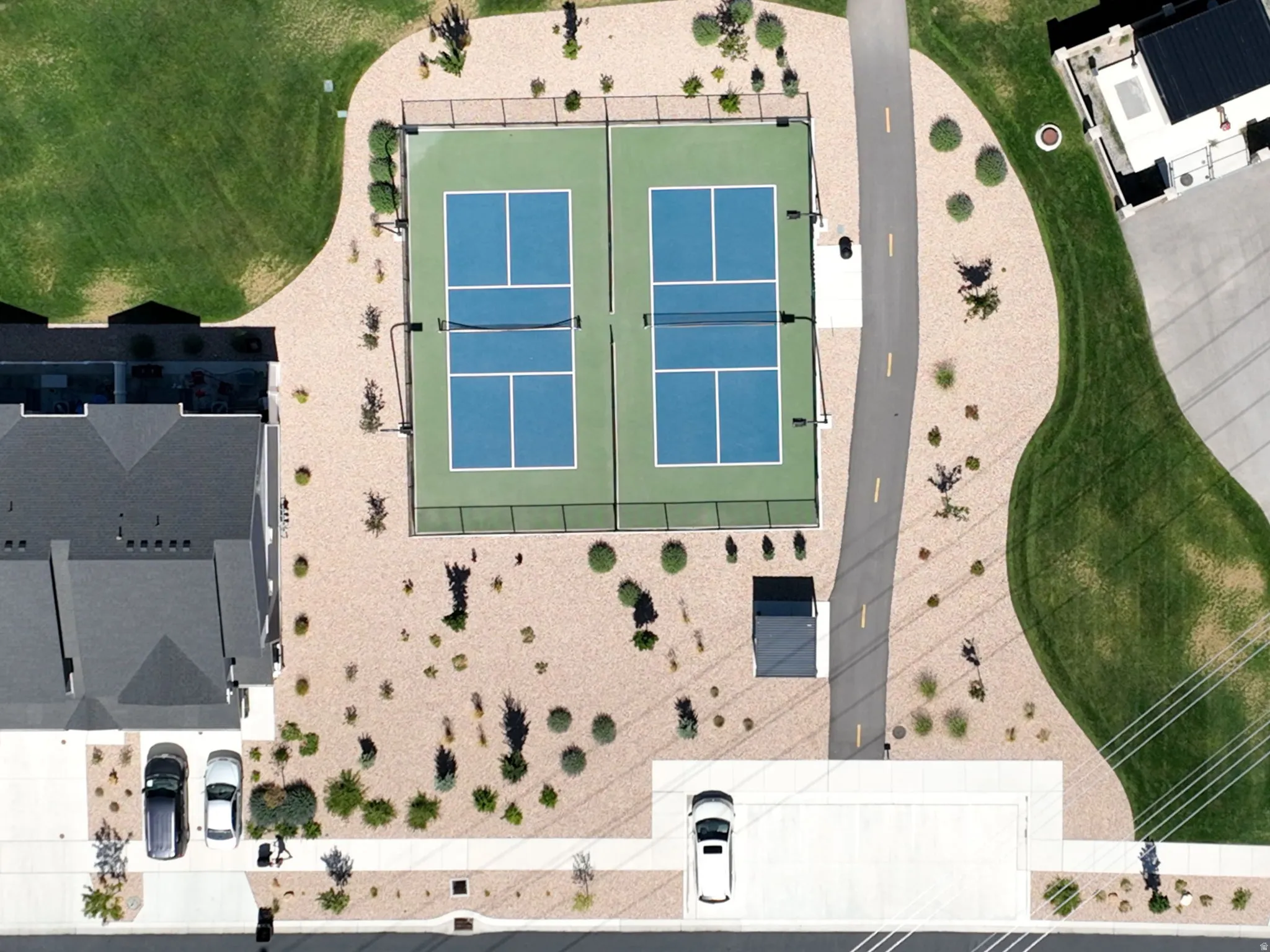 Two pickleball courts with perimeter fencing, surrounded by xeriscaping, and a paved pathway