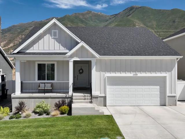 Light gray exterior siding with white trim, covered front porch, attached garage, and mountain backdrop
