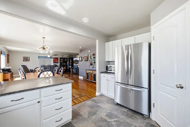 White cabinetry, stainless steel refrigerator, stone tile flooring, recessed lighting, and wood-finish flooring