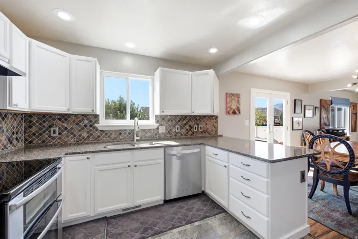 White cabinetry with dark hardware, stone countertops, mosaic tile backsplash, and a stainless steel dishwasher