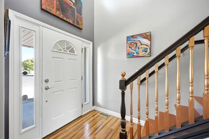 Hardwood flooring, white entry door with side lites, half-round transom, and a staircase with a black handrail and golden balusters