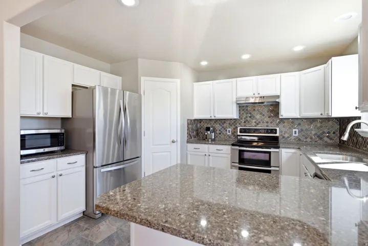 White cabinetry, stainless steel appliances, mosaic tile backsplash, granite-style countertops, and recessed lighting