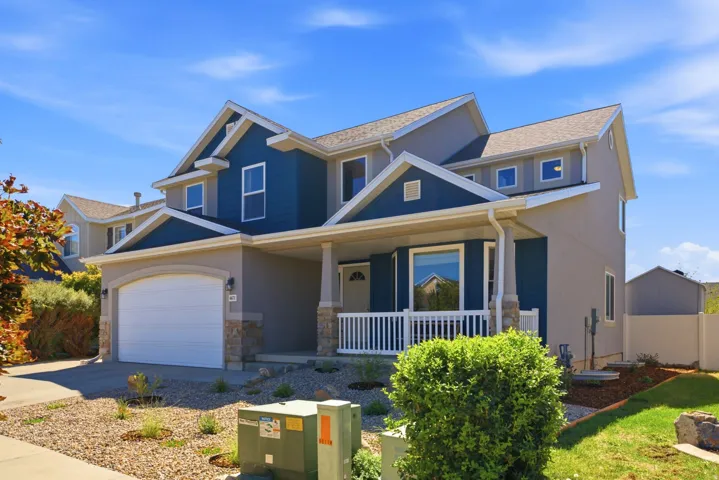 Two-story residence featuring a covered front porch, attached garage with a white door, and a multi-toned exterior with blue and gray siding