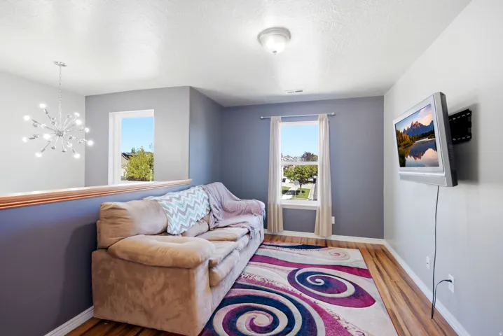 Wood-finish flooring, two windows with natural light, a contemporary chandelier, and a wall-mounted television bracket
