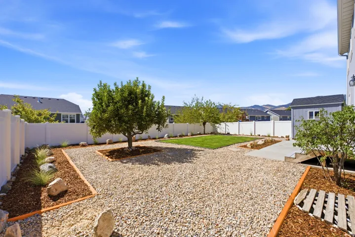 Expansive backyard featuring a white vinyl privacy fence, gravel landscaping with wood mulch accents, mature trees, and a manicured lawn area
