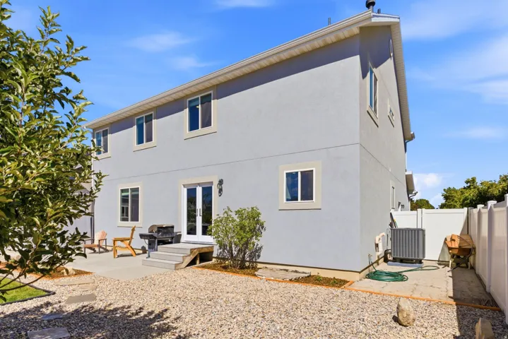 Stucco exterior with multiple windows, second-story fenestration, ground-level patio access, and a gravel-covered yard