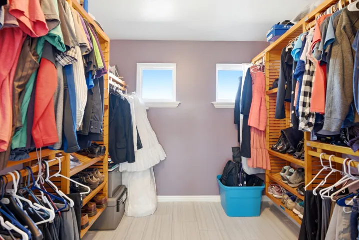 Custom closet system featuring wood shelving, multiple hanging rods, and light-colored flooring
