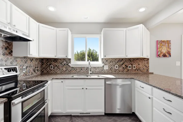 White cabinetry, stainless steel appliances, mosaic tile backsplash, countertop surfaces, and recessed lighting