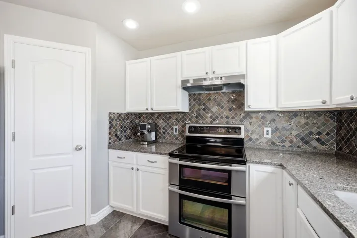 White cabinetry with brushed nickel hardware, patterned tile backsplash, solid surface countertops, stainless steel double oven range, and recessed lighting