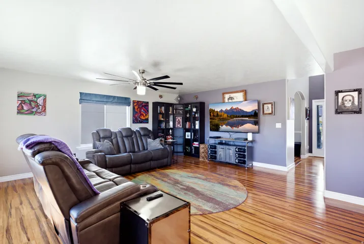 Spacious living area featuring wood-finish flooring, a ceiling fan with integrated lighting, and a corner built-in shelving unit
