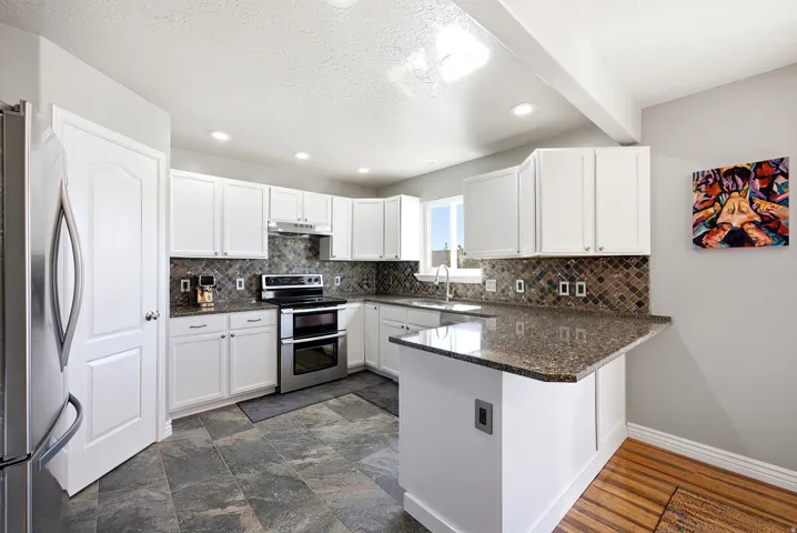 Kitchen featuring white cabinetry, stone-finish countertops, stainless steel appliances, and a mosaic tile backsplash