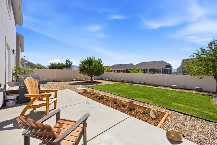 Expansive concrete patio with a manicured lawn, established tree, and decorative rock landscaping