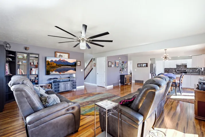 Open-concept living space featuring wood-finish flooring, a contemporary ceiling fan with integrated lighting, and a built-in display cabinet