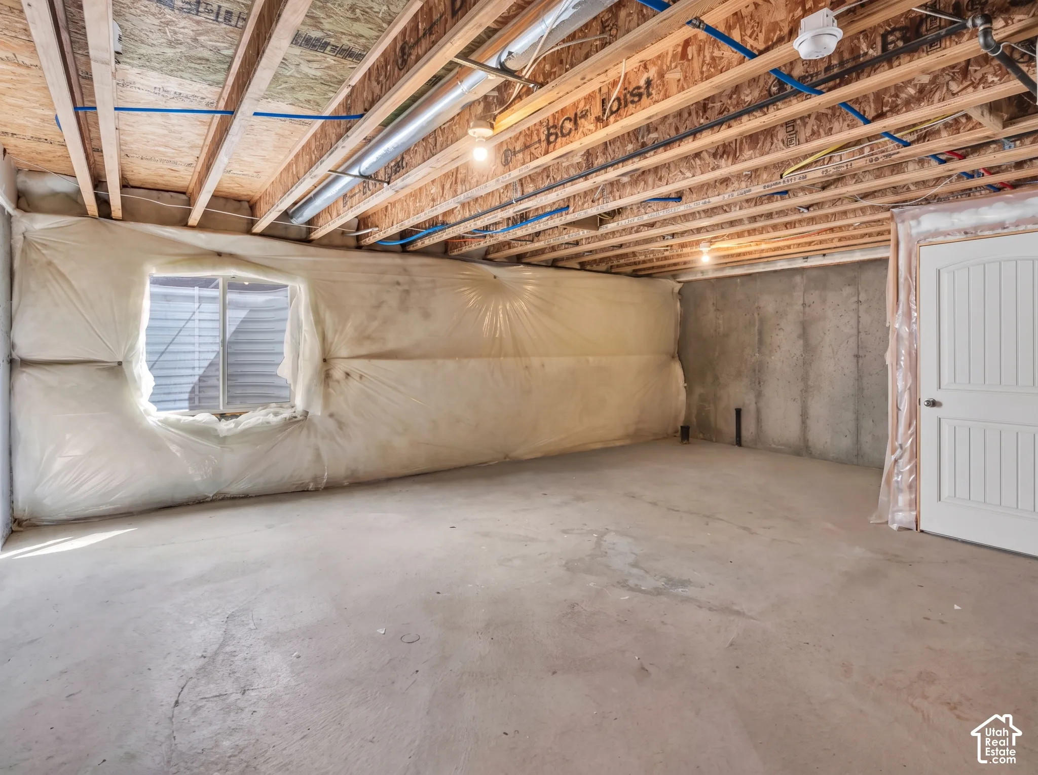 Daylight basement with an egress window, concrete foundation walls, exposed ceiling joists, and a panel door
