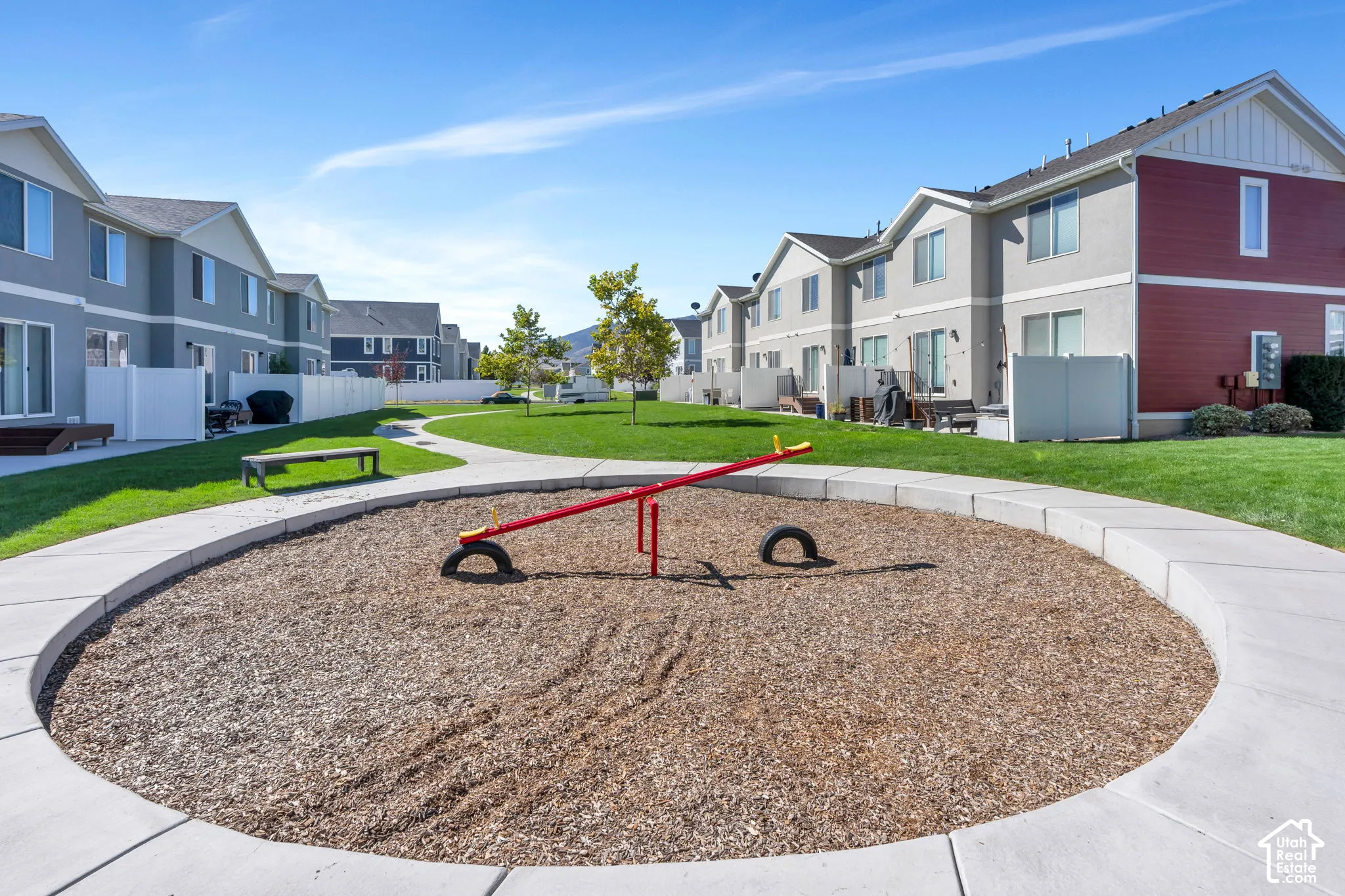 Manicured green spaces with a winding pathway, playground area featuring a seesaw, and private backyard patios