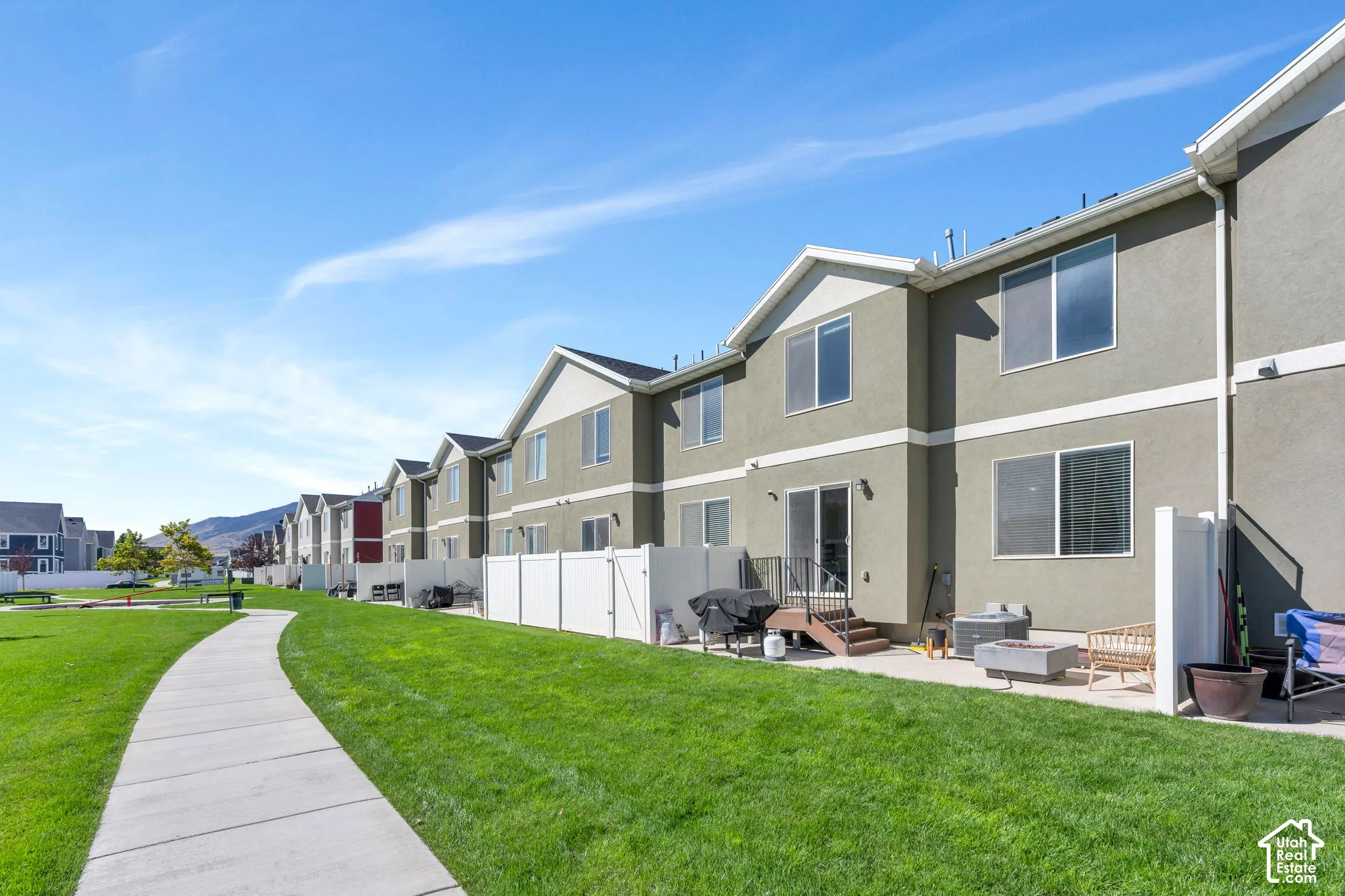 Expansive green space with a concrete pathway, private patio, and sliding glass door access