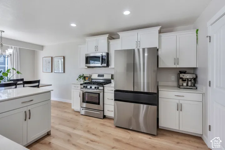 White shaker-style cabinetry with stainless steel appliances, light wood-finish flooring, recessed lighting, and light-toned countertops