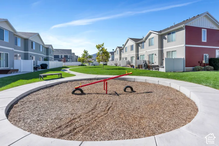 Manicured green spaces with a winding pathway, playground area featuring a seesaw, and private backyard patios