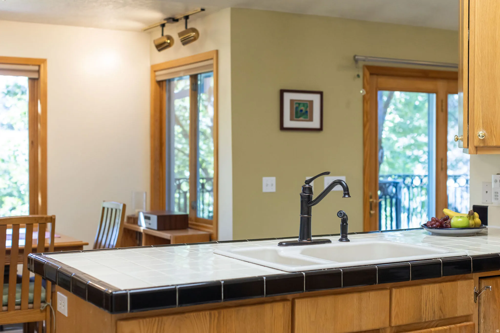 Ceramic tile countertop with black trim, stainless steel double basin sink, and oil-rubbed bronze faucet