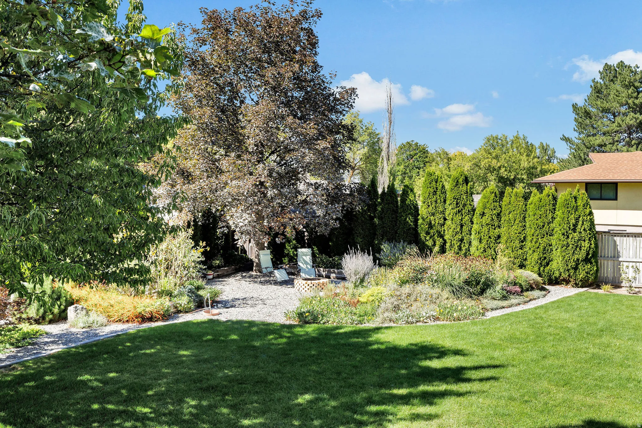 Expansive backyard featuring a manicured lawn, established perimeter landscaping, and a gravel patio area