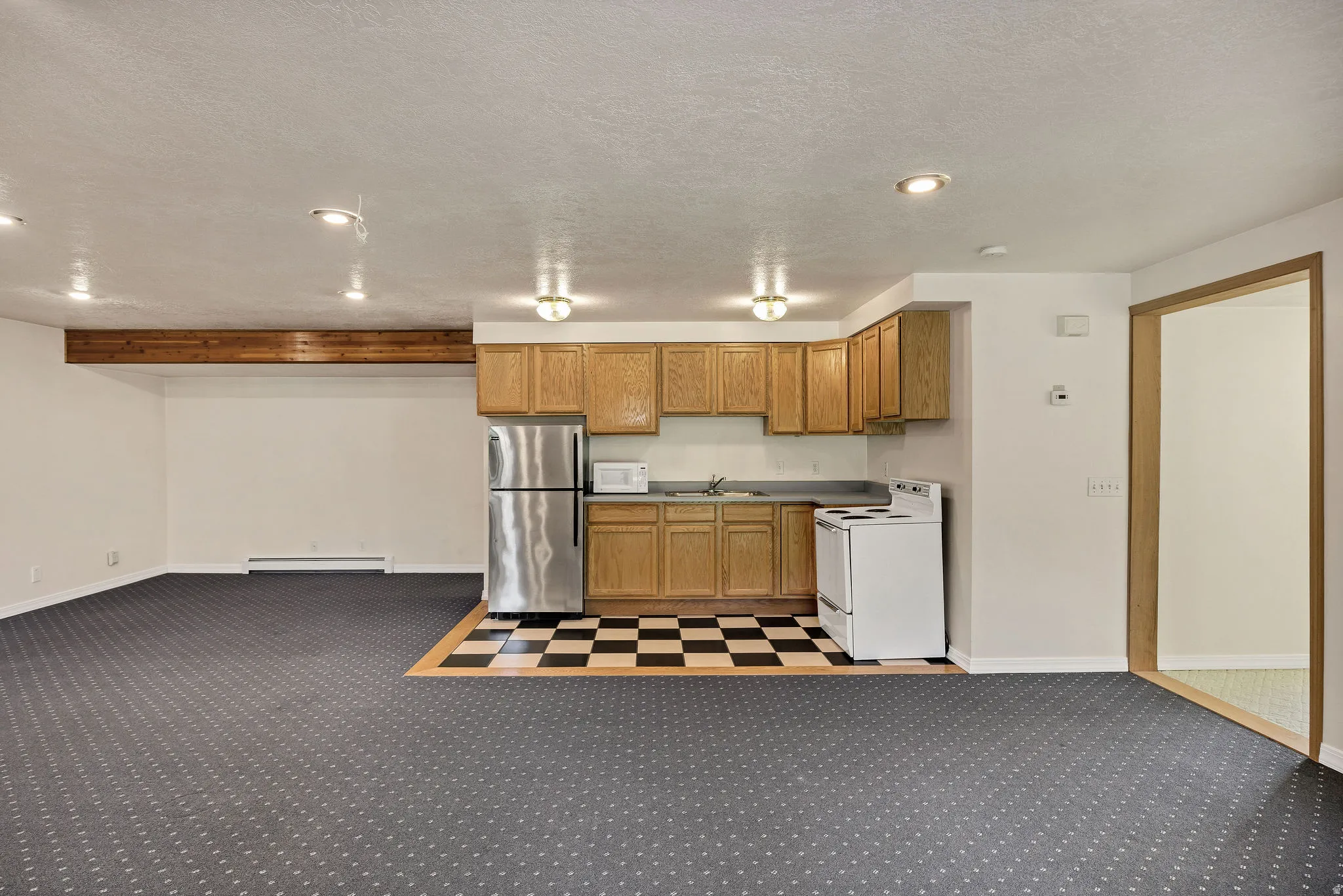 Recessed lighting, wood-finish beam, wood cabinetry, stainless steel refrigerator, and checkered floor tile