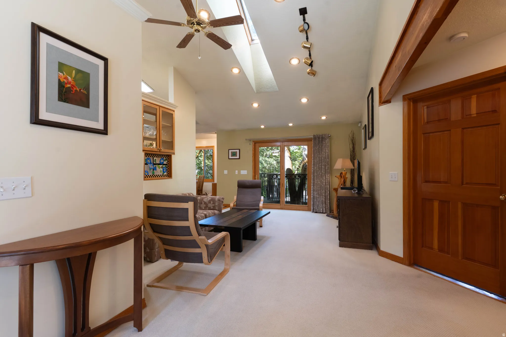Vaulted ceiling with skylight, recessed lighting, wood-paneled door, exposed wood beam, and glass-paneled patio doors
